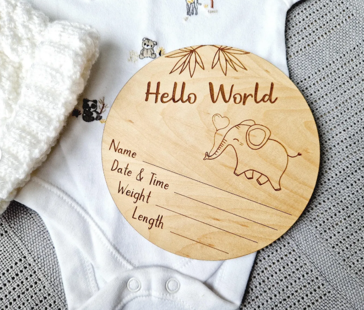 A wooden baby name card with a picture of an elephant and the text "Hello World" is placed on a white cloth.